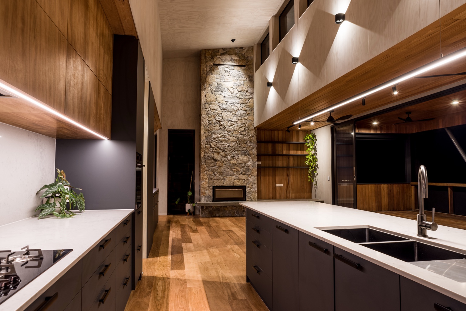 Trees Road kitchen with timber joinery, a high ceiling and a full-height stone fireplace.