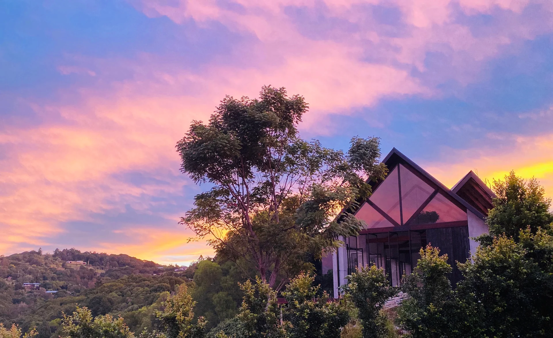 Warri Way’s gabled exterior among the trees in Currumbin Valley beneath a pink and gold sunset.
